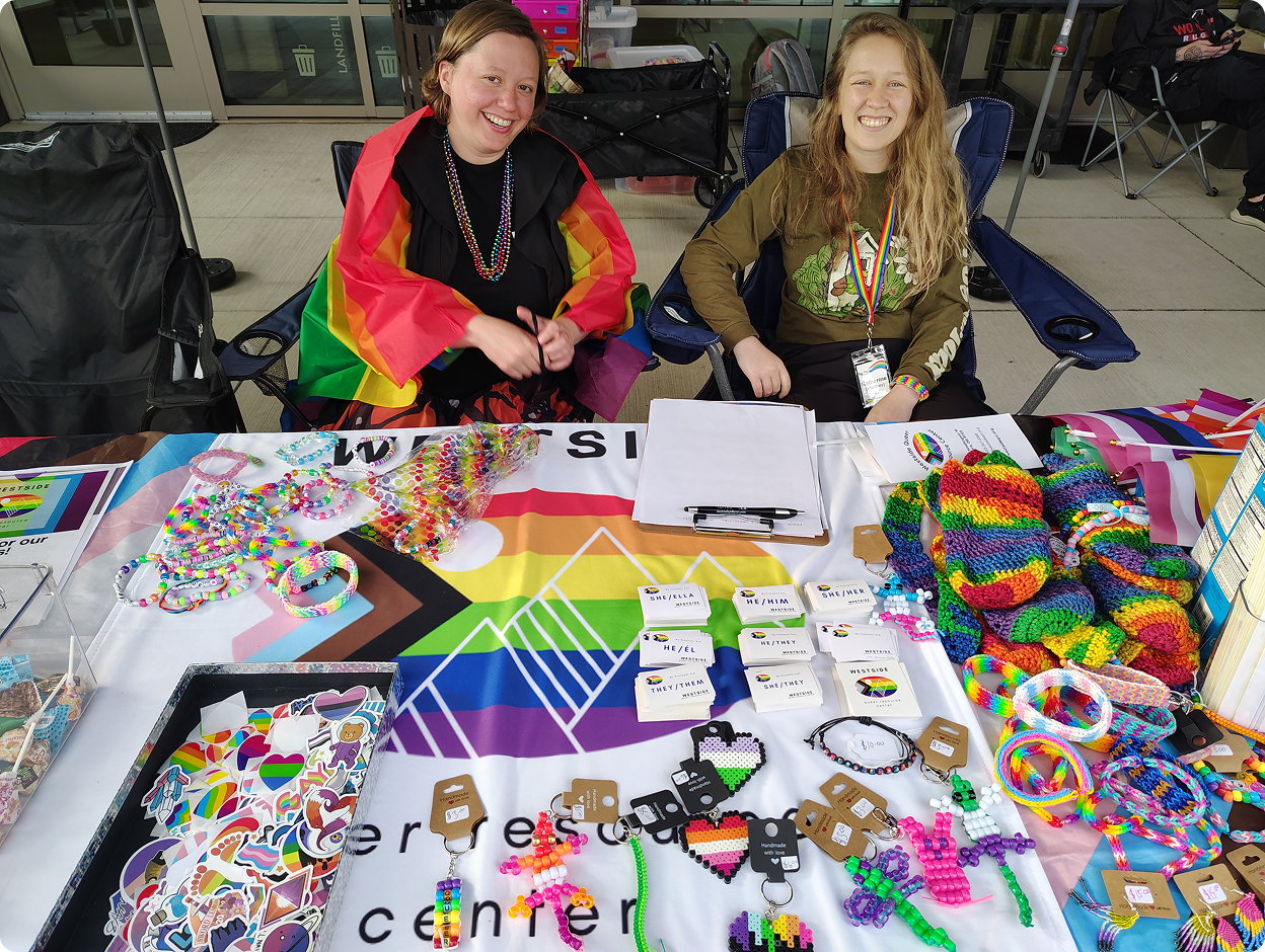 Two smiling volunteers are sitting at a table filled with things to engage the community with